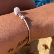 Shell bracelet and abalone pearl on a leather link worn on a wrist with a tattoo